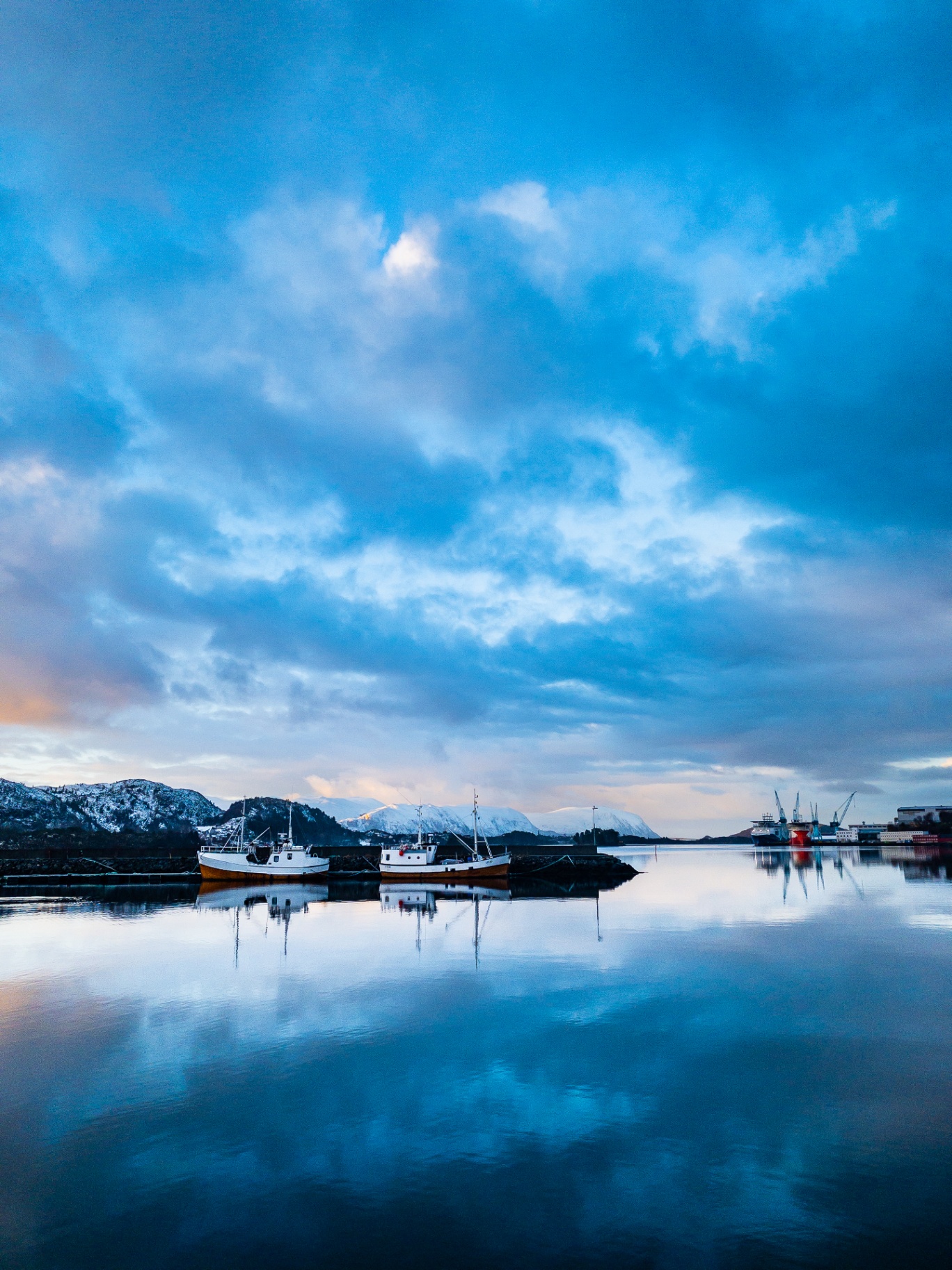Fjord med båtar og snødekte fjell i blått morgonlys